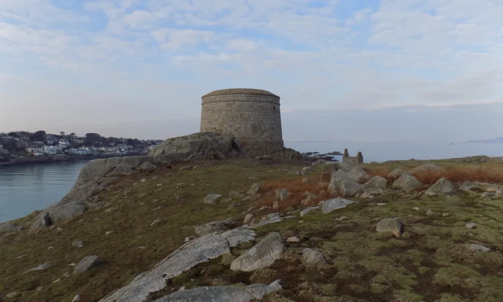 Stone tower on a rocky hill overlooking the sea with a coastal town in the background