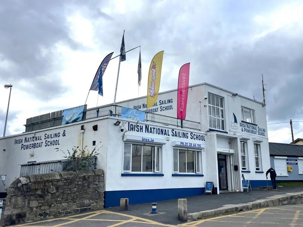 Exterior view of the Irish National Sailing & Powerboat School building with signage, flags, and contact details visible