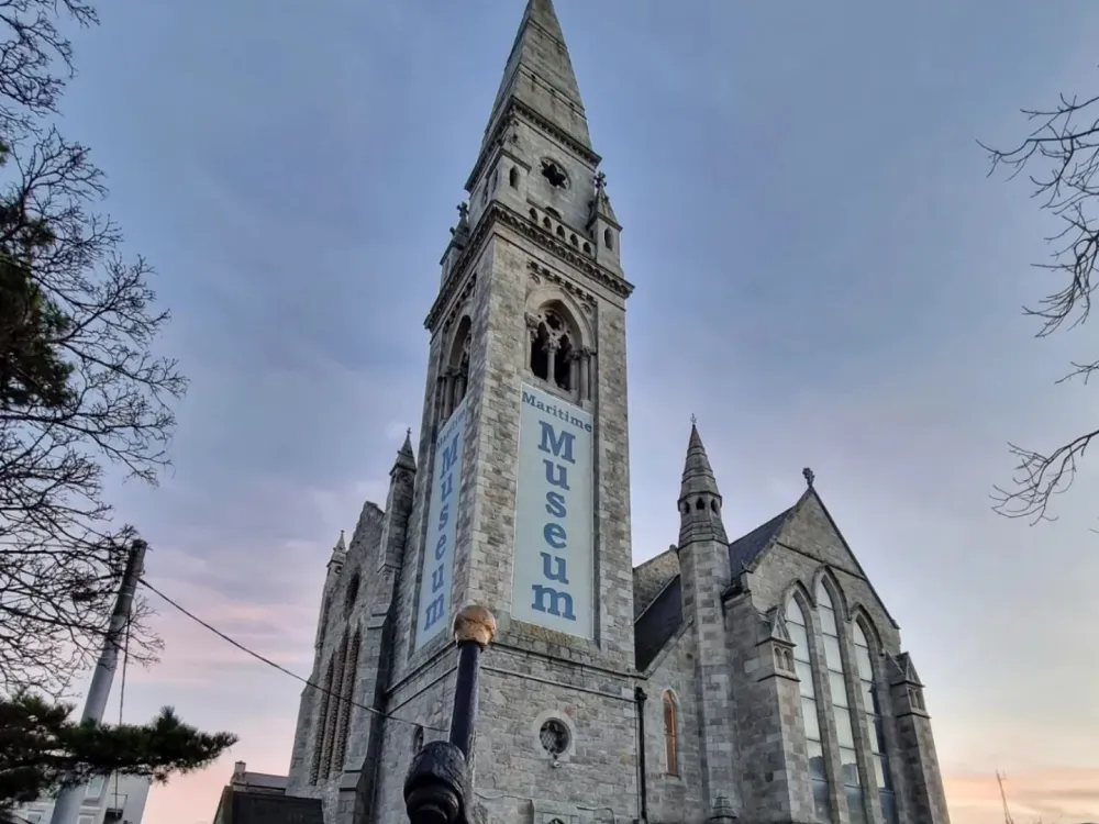 Historic stone building with Gothic architecture and banners reading “Maritime Museum,” captured under a sunset sky